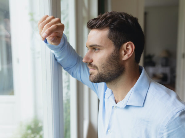 Side view of thoughtful Caucasian man looking outside through window in a comfortable home